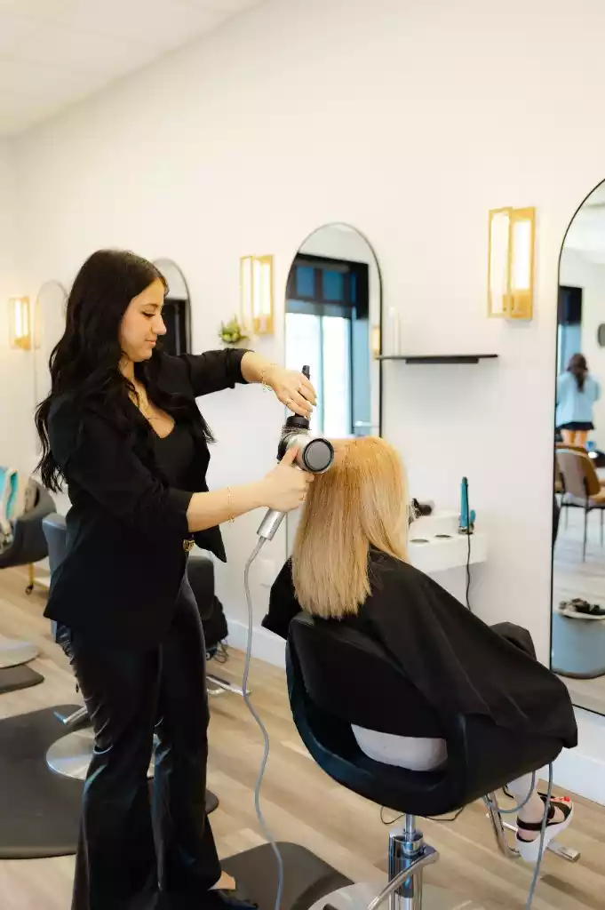 A Maxima Hair stylist blow-drying a blonde client's hair in the salon