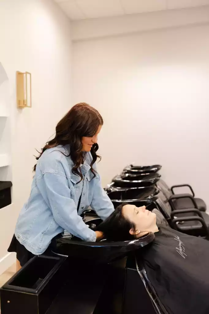 A stylist washing a client's hair at the salon's shampoo station